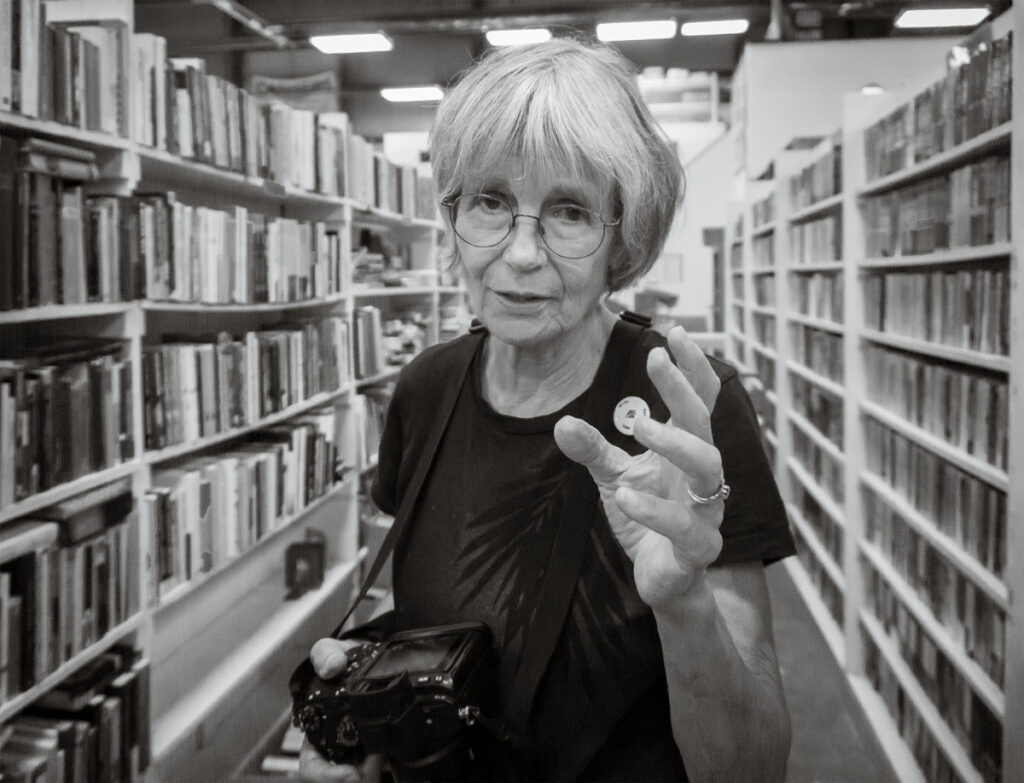Kris Altucher • <em>Susan Larkin at Friends of the Library Book Sale</em> • Archival digital print • 13″×10″ • $60.00