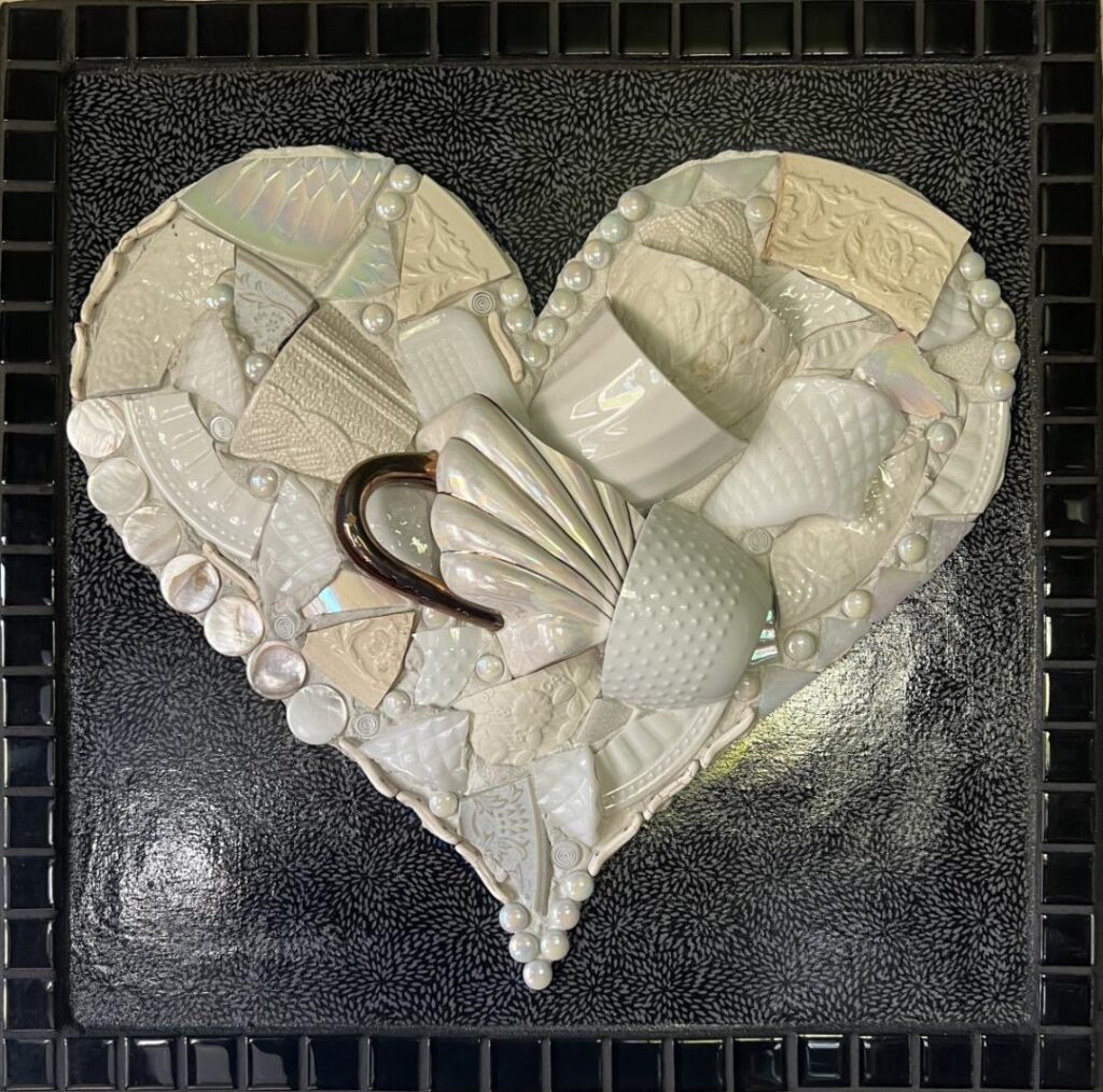 Peggy Ahouse • <em>Pieces of My Heart</em> • Cups , dishes, fabric, buttons and various found objects with a glass tile boarder. • 18″×18″ • $550.00