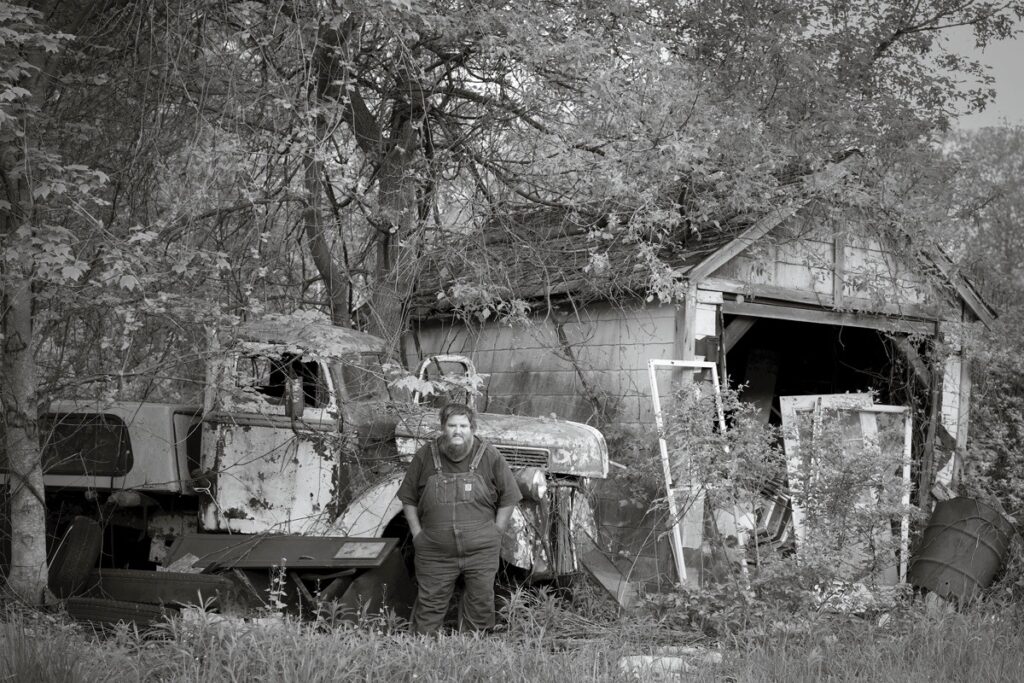 Susan C. Larkin • <em>Nate Jr. with his Old Ford and the Garage that was Moved</em> • Archival metal print • 36″×24″ • $400.00