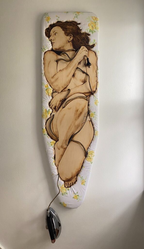 Chelsea Hagin&nbsp;• <em>Don't Trad On Me</em>&nbsp;• Mixed media—pyrography on wood, fabric, color pencil, coffee, vintage iron and cord&nbsp;• 16″×&nbsp;63″&nbsp;• $2,000.00<a class="purchase" href="https://state-of-the-art-gallery.square.site/product/chelsea-hagin-don-t-trad-on-me/EDZRRL3FHWIBKXUSUWVJHAKK" target="_blank">Buy</a>